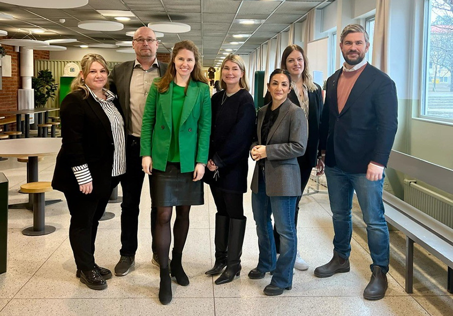 Fem kvinnor och två män står bredvid varandra i en skolbyggnad. Alla ler glatt och tittar in i kameran. 