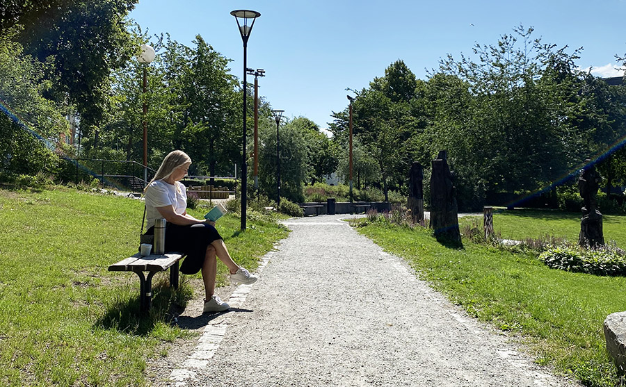 Kvinna sitter på parkbänk vid grusad väg och läser