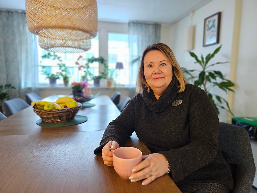 Ann-Charlotte Tjernberg sitter med en kaffemugg vid ett fikabord med fruktskålar på bordet.