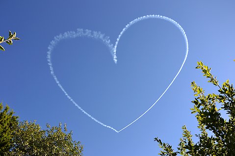Rökmoln efter flygplan som format ett hjärta på himlen.