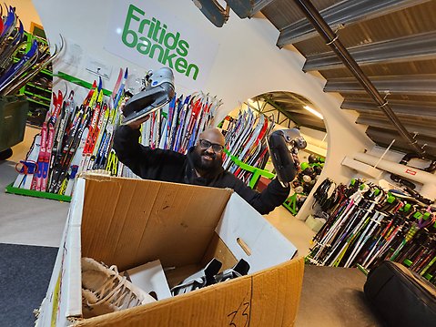 En man håller upp två skridskor ovanför en flyttkartong i Fritidsbankens lokaler.