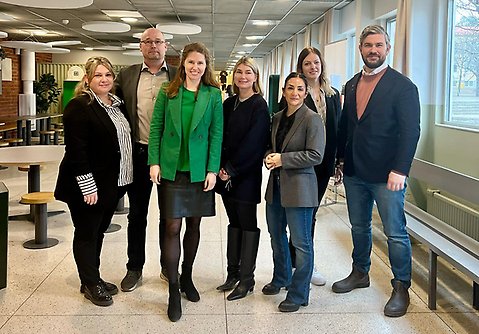 Fem kvinnor och två män står bredvid varandra i en skolbyggnad. Alla ler glatt och tittar in i kameran. 